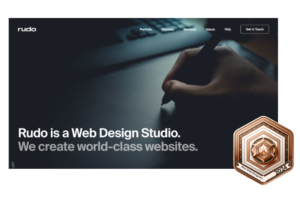 Best web designers 2024 bronze award badge on the homepage of Rudo, a web design studio, with a tagline stating they create world-class websites, depicted alongside a designer's hand working on a graphics tablet.