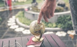 A hand pressing a small globe on top of a passport illustrating international travel and expansion 