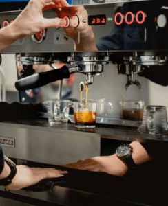 A barista adjusting the controls of a professional espresso machine while fresh espresso pours into a measuring jug